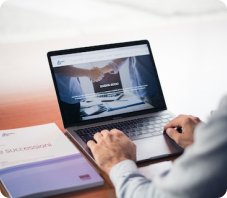 Person working on a laptop with a handshake image on the screen, indicative of a successful deal or partnership, with business documents on the desk
