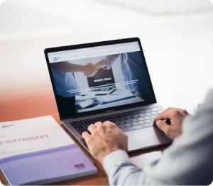 Person working on a laptop with a handshake image on the screen, indicative of a successful deal or partnership, with business documents on the desk