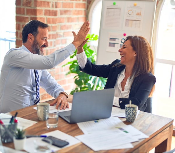 Two professionals celebrating success with a high-five over a work desk in a bright office setting