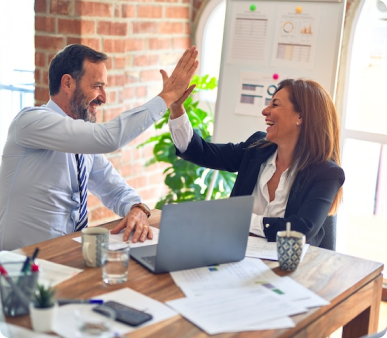 Two professionals celebrating success with a high-five over a work desk in a bright office setting